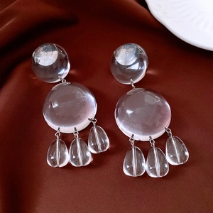 Detail view of transparent resin round earrings with teardrop pendants on brown silk