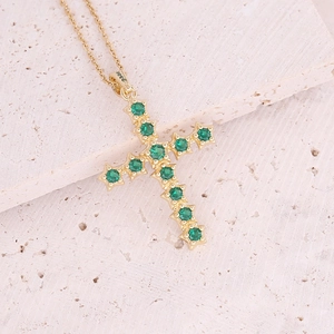 18K gold plated copper cross pendant necklace with green zircons on a stone background
