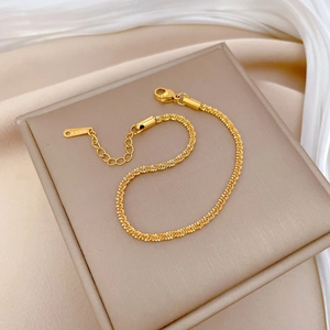 Detail shot of a delicate gold titanium steel chain bracelet on a brown leather display