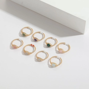 Set of eight handmade wire-wrapped gold rings with assorted colorful gemstones on white blocks