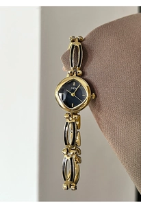 Detailed close-up of GEDI gold chain watch with black enamel links on wool fabric
