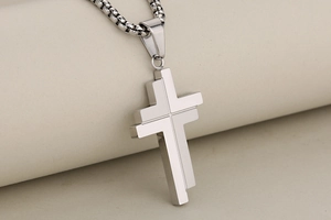Close-up of a silver multi-layered geometric cross pendant necklace on a beige roll paper