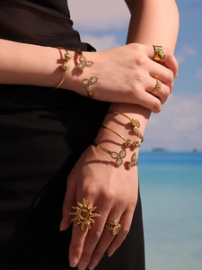 Detail shot of gold-plated bracelets and rings with zircon charms on a beach background