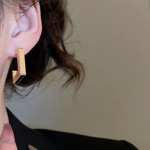 Close-up of a model wearing a geometric gold C-shaped earring with a polished metal finish