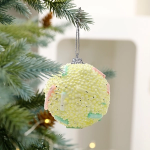 Macaron yellow foam Christmas ball with colorful accents hanging on green tree branch