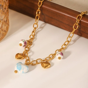 Detail of golden chunky chain necklace with heart charms and floral beads on a white surface