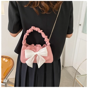 Detail of pink pleated handbag with large white bow decoration and gold chain strap