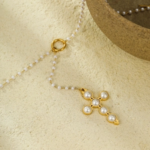 Vintage stainless steel cross pendant necklace with pearls on an elegant textured backdrop