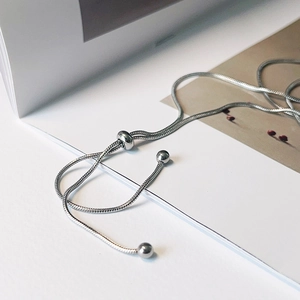 Macro detail of silver adjustable snake chain necklace with round beads on book