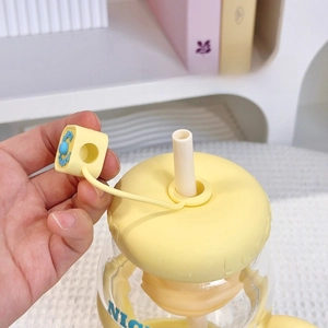 Close-up of yellow silicone straw dust cap with anti-lost strap on clear glass bottle