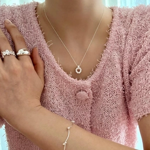 Close-up of minimalist 925 sterling silver necklace and rings worn on a soft tweed jacket