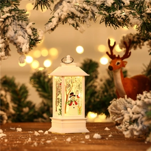 Detail of white Christmas LED lantern with snowman scene against snowy pine branches