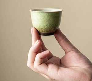Detail of hand holding a bell-shaped ceramic teacup with green kiln-altered glaze