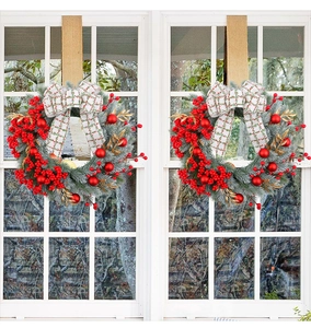 Detail of two Christmas wreaths with red berries, gold leaves, and checkered bows on windows