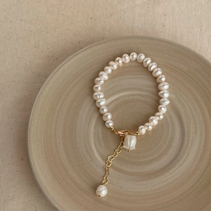 Detailed close-up of Baroque pearl bracelet with golden tulip charm on ceramic plate