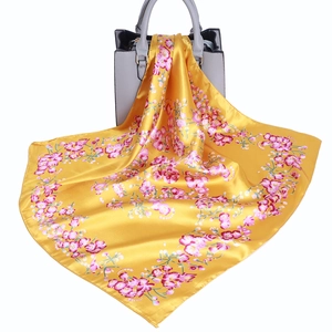 Yellow floral satin square scarf with colorful flower pattern tied to a leather handbag
