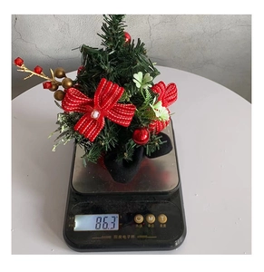 Close-up of a mini Christmas pine tree with red berries and bowknot decoration on a scale