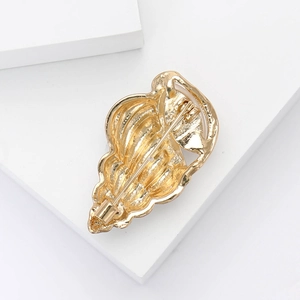 Macro shot of gold alloy conch brooch showing detailed texture and back safety pin