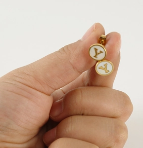 Close-up of golden letter Y earring with white shell inlay held by hand for scale