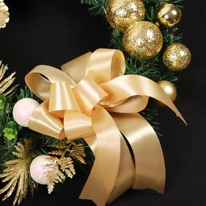 Golden Christmas wreath with champagne satin bow, pine needles and ornaments on black background
