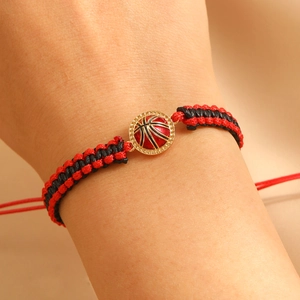 Detail van handgeweven rood en zwart basketbalarmband om pols met gouden bedel