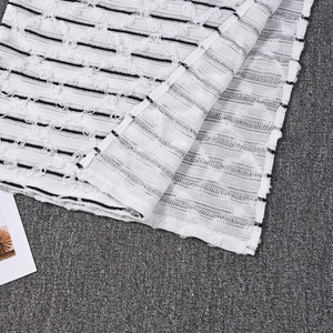 Macro shot of white knit fabric with black stripes and 3D floral pom-pom textures
