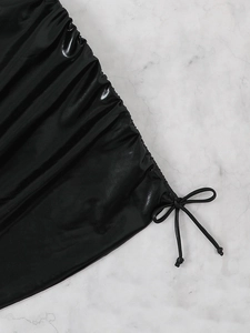 Close-up of black glossy ruched bikini fabric with tie-up bow detail and leather texture