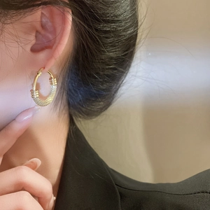Close-up of textured golden titanium steel hoop earring worn by a model in a side view