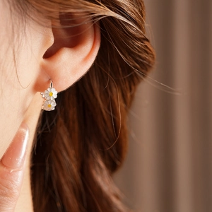 Close-up of silver vintage enamel daisy hoop earrings worn on ear with yellow center