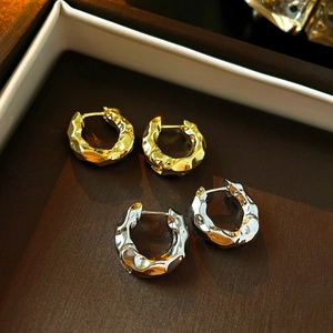 Minimalist gold and silver hoop earrings with irregular hammered metal texture on tray