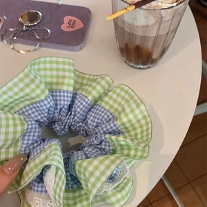 Détail d'un chouchou à carreaux avec dentelle tenu à la main sur une table de café
