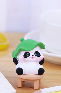 Macro shot of a cute panda figurine wearing a green lotus leaf hat on a mini wooden stool