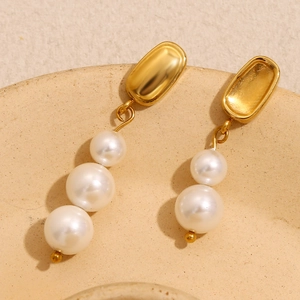 Détail macro de boucles d'oreilles asymétriques plaquées or 18K et perles blanches