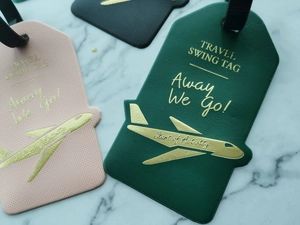 Flat lay of pink and dark green airplane-shaped leather luggage tags on marble background