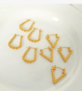 Macro detail of gold beaded geometric earrings arranged in a white ceramic dish