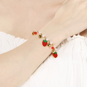 Detailed view of gold fruit charm bracelet with red strawberry, heart and white pearl charms
