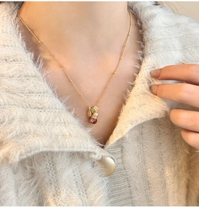Close-up of 18k gold-plated lucky bag necklace with red beads and pearls on white sweater
