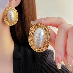 Close-up of vintage gold pleated oval earrings with pearl center on a person's ear