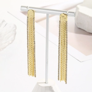 Macro detail of long gold tassel earrings with rhinestones on a minimalist stand