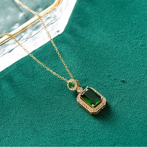Detail of emerald cut green gemstone pendant with micro-pave diamonds on golden chain