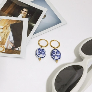 Dettaglio di orecchini vintage dorati con pendente in ceramica floreale bianca in stile lifestyle