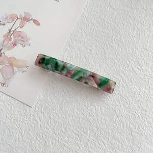 Detail of a rectangular acetate hair clip featuring colorful marble texture and silver metal base