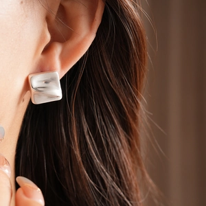 Close-up of minimalist silver wavy square stud earrings worn by a model in detail