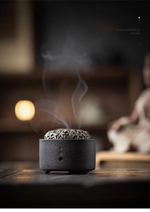 Close-up of matte black ceramic incense burner with golden hollow lid and rising smoke