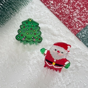 Detail of glittery Santa Claus and Christmas tree hair claws on snow with pine branches