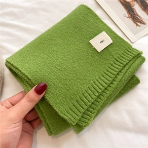 Close-up of green knitted scarf with soft rib texture and a minimalist 'emo' label