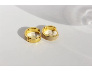 Vista macro de pendientes huggie dorados en forma de C con detalles de esmalte beige