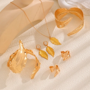 Golden leaf jewelry set with necklace, earrings, open bracelets and rings on beige texture