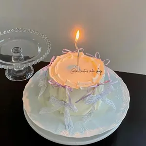 Close-up of cream cake with purple silk bows and a silver wavy candle on a glass tray