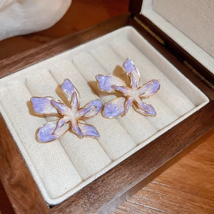 Gros plan détaillé de boucles d'oreilles fleurs dégradé violet avec bords dorés dans un coffret